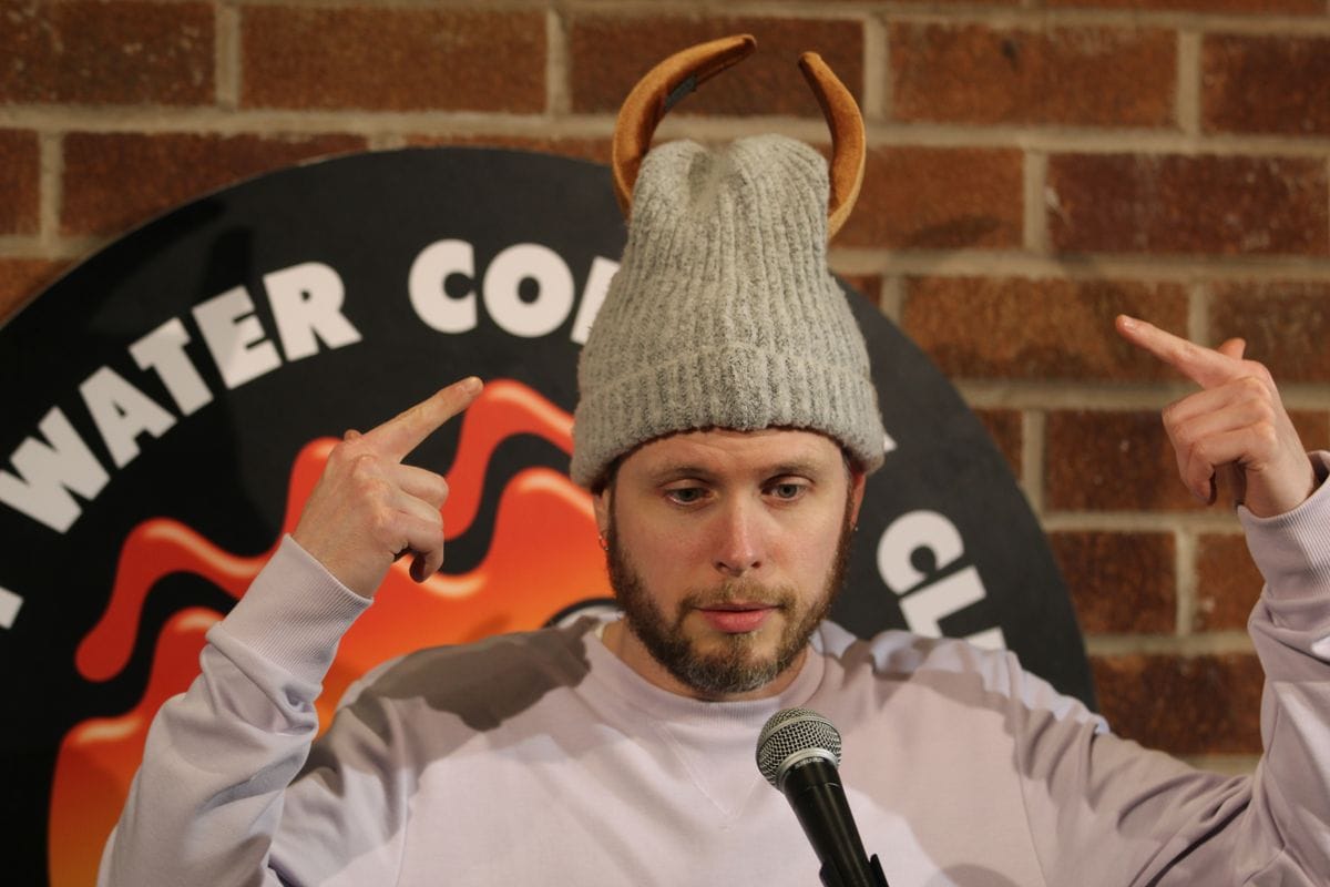 Phil Chapman at Hot Water Comedy Club in a knitted hat with horns, pointing at them with both hands