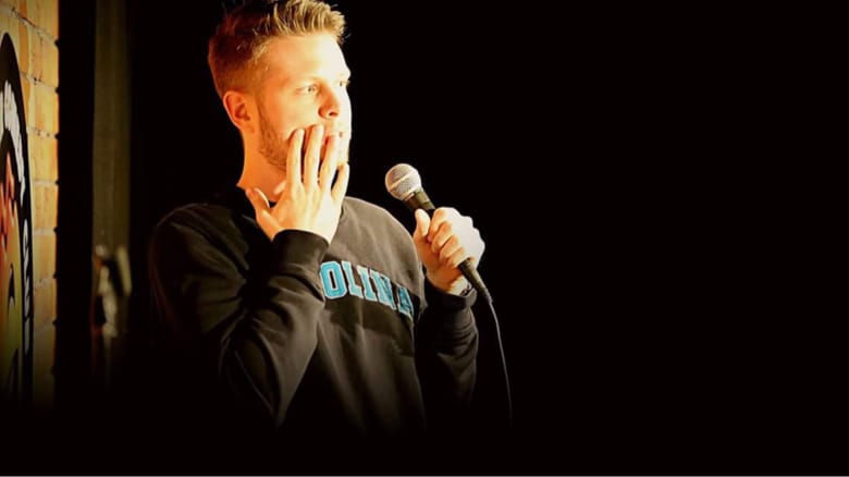 Phil Chapman in a single spotlight, hand to his mouth in mock horror